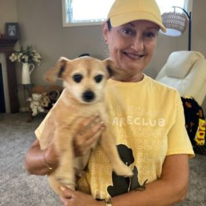 Pet care professional Kim holding a small tan dog in her arms indoors.